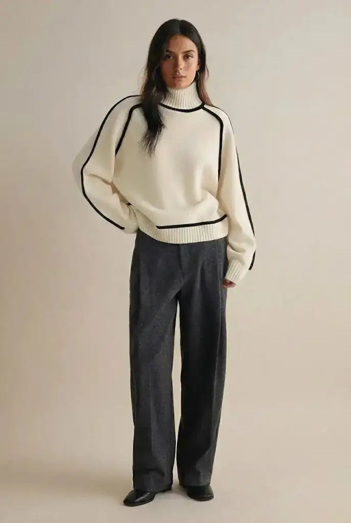 Cream-colored turtleneck sweater with black contrast stitching along the shoulders and hem.
