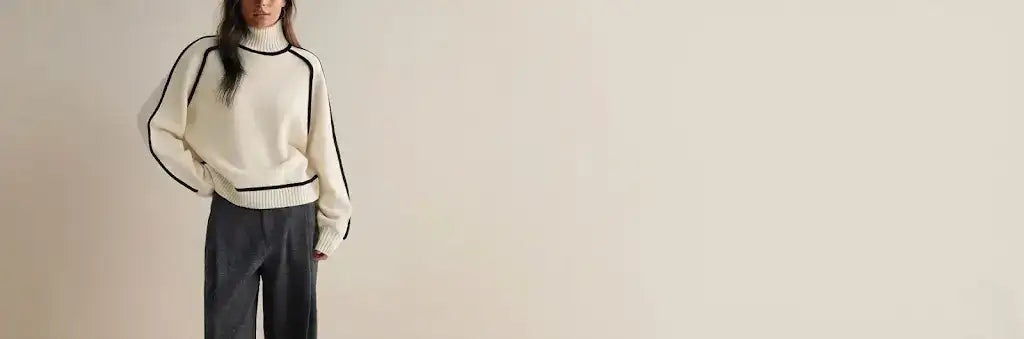 Cream-colored turtleneck sweater with black contrast piping along the sleeves and hem.